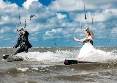 Braut und Bräutigam fahren beim Kitesurfen über das Wasser während eines kreativen Hochzeitsfotoshootings