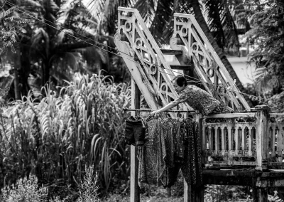 Frau hängt Kleidung auf Balkon in tropischer Umgebung Schwarz-Weiß